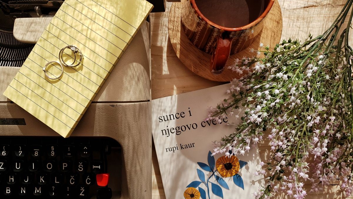 Charming vintage flatlay with a typewriter, coffee mug, flowers, and rings on a wooden surface.